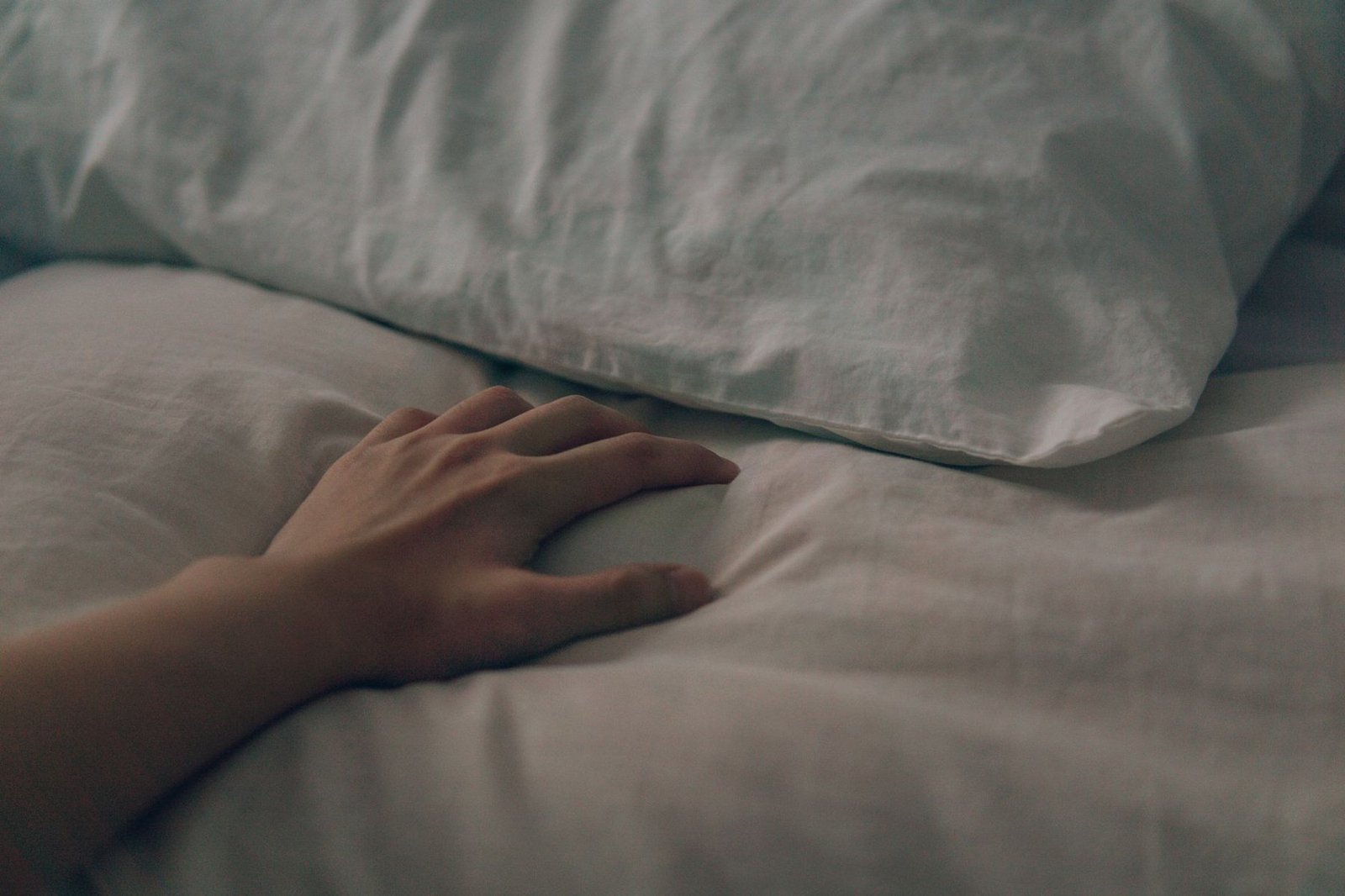 A hand resting softly on a bed by a pillow