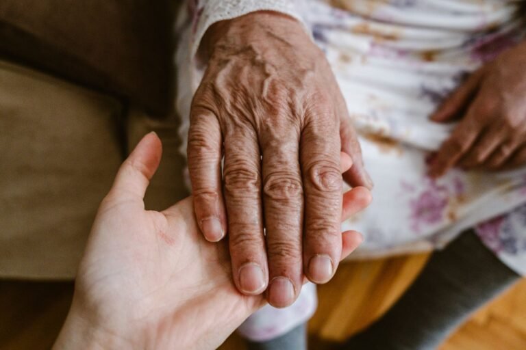 A younger hand gently holding the hand of an older person